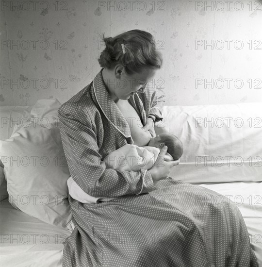 1950s mother nursing her baby. A young woman breastfeeding her baby at home. Sweden 1951 Neg CV/24