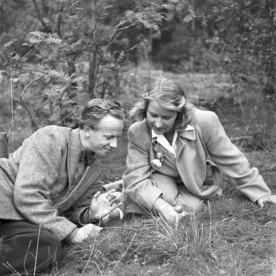 Couple in the nature. A young couple pictured sitting on the ground looking at a mushroom. Sweden 1944. Kristoffersson Ref M20-2