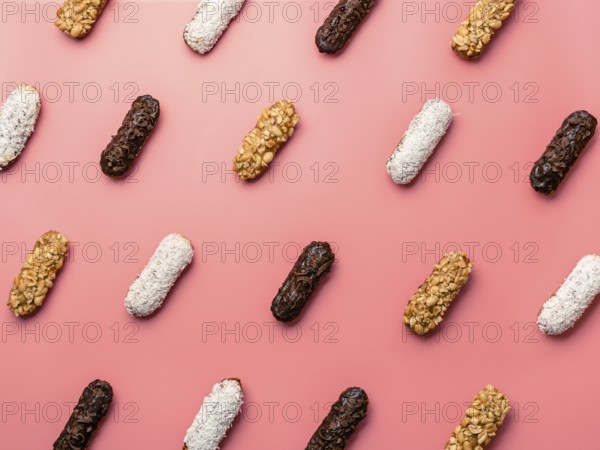 Pattern of different homemade eclairs on pink background. Top view of delicious healthy profitroles with different decor - chocolate, peanut and sherdded coconut