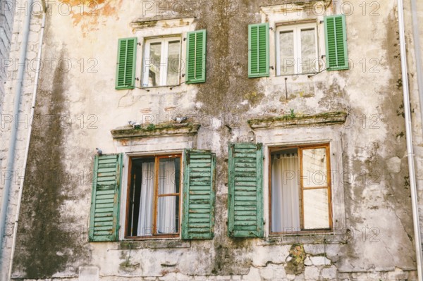 An old multi-storey building with windows and wooden shutters with peeled paint.