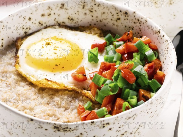 Savory oatmeal in craft trendy bowl, served with vegetables and fried egg on white concrete background. Red bell pepper and bunch onion on background