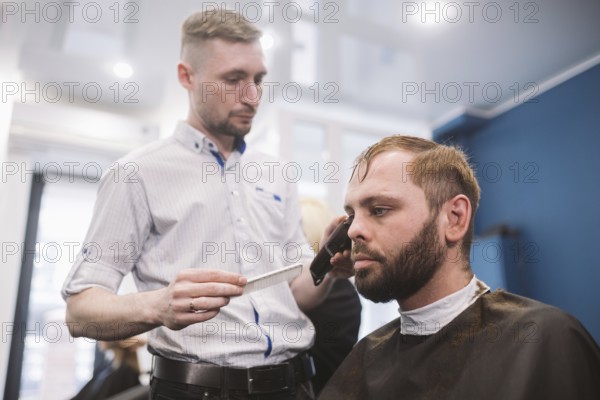Close up shot of a man getting a trendy haircut at a hair salon. Male caucasian hairdresser serving a client. Man with a beard making haircut with a typewriter and comb