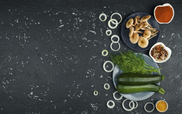 Fresh zucchini, mushrooms, spices and herbs on a black board. View from above. Copy space