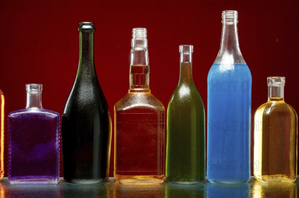 Verschiedene alkoholische Getränke in transparenten Flaschen auf rotem Hintergrund