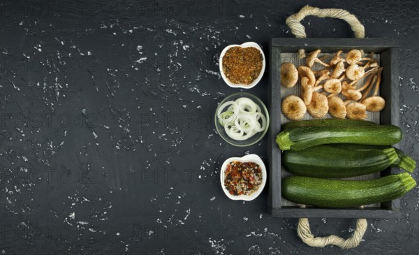 Fresh zucchini, mushrooms, spices and herbs on a black board. View from above. Copy space