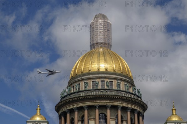 Historic building with golden dome and a passing aeroplane in the blue sky with clouds, saint petersburg, baltic sea, russia