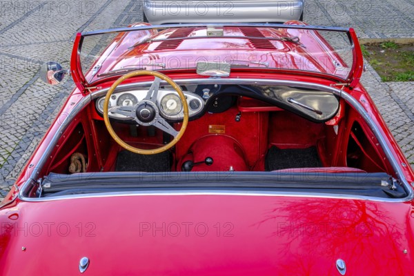 Lisbon, Portugal, Jan 20, 2024: Original red interior of red Austin-Healey 100 vintage convertible sports car parked on cobblestone pavement road. Red velvet and leather, wooden steering wheel, fold-down windshield, Europe