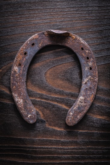 Rusty longstanding horsehoe on vintage dark wooden board construction concept
