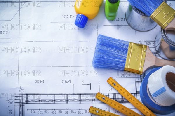 Duct tape safety gloves wooden meter and paint brush cans bottles on blueprint maintenance concept
