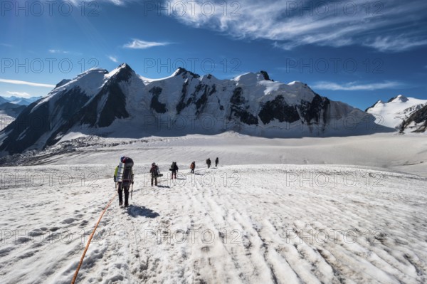 Group of Mountaineers with Backpacks is Roped Together and Ascending on Glacier in Snowy Mountains