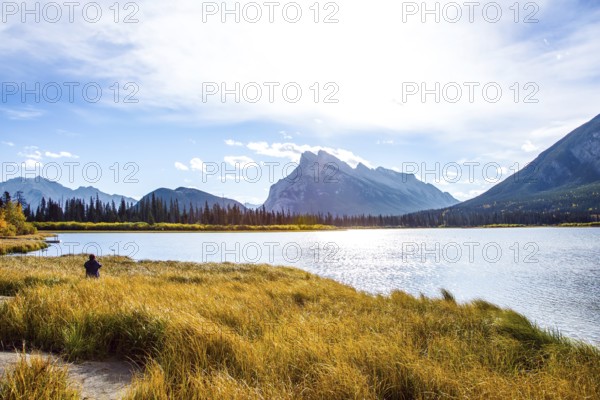 Woman photographing a magnificent lake in the Rocky Mountains of Canada. Travel to autumn. Lake Vermillon among the yellow fall foliage of birches and aspens. The concept of photo tourism