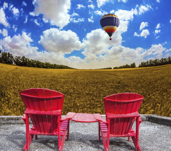 Huge balloon flies over a field. Convenient red chairs in a wheat field. The concept of eco-tourism. Rustic vacation