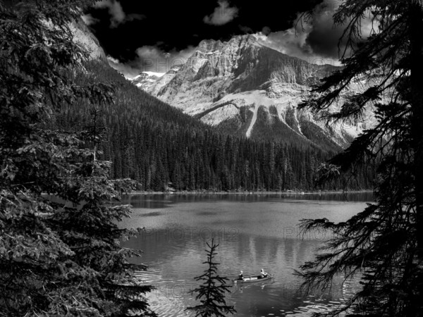Two people paddle in a canoe on Emerald Lake surrounded by the Canadian Rocky Mountains and thick forests inside Yoho National Park in British Columbia, Canada, North America