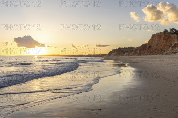 The golden sandy beach of Praia da Falésia, crystal clear sea water at low tide with the reflection of the sky, the setting sun and the characteristic orange-coloured cliffs, Algarve, Portugal, Europe