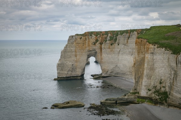 Landscape photo of tall, steep limestone cliffs by the ocean with one with a hole in it creating an arch