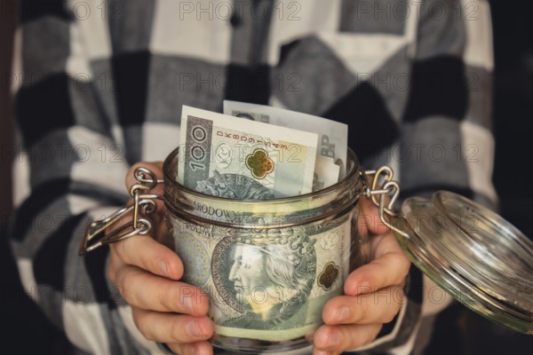 Polish zloty banknote saving money in glass jar. Unrecognizable woman moderate consumption and economy Collecting money. Tips. Business, finance, saving, banking and people concept. Extra money, passive income. Saving for travel, crisis, house, car, education, retirement
