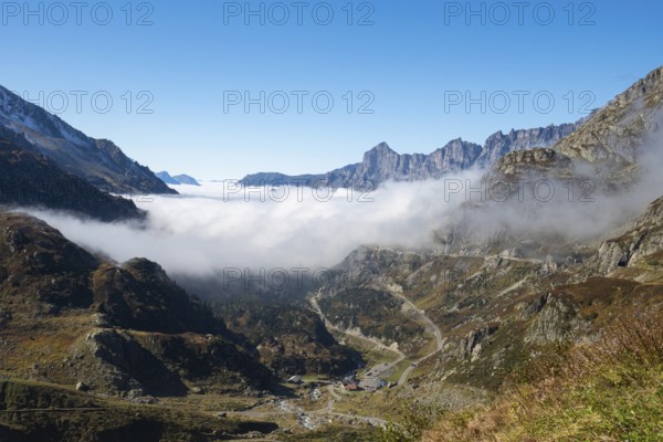 Situation on Susten pass on a sunny autumn day. View into the valley filled with fog with the pass street