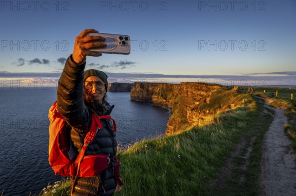 Female hiker taking a selfie, Cliffs of Moher, The Burren, County Clare, Ireland, United Kingdom, Europe