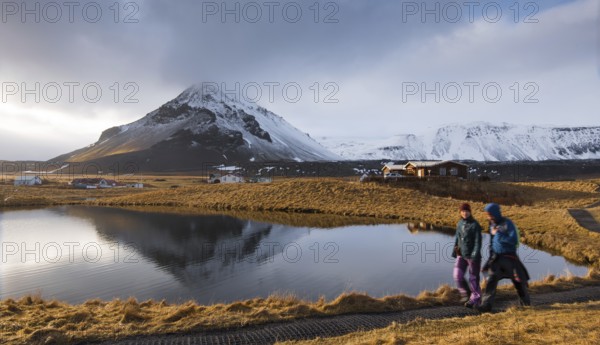 Arnarstap, Iceland, March 21 2016: People walking around a lake with snowy mountain reflected on the water at Arnarstapi area in Snaefellsnes peninsula in Iceland, Europe