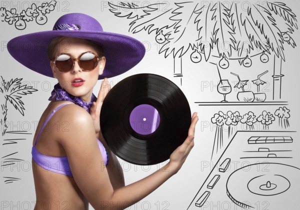 Colourful photo of a beautiful DJane in a bikini holding a retro vinyl record in her hands on a sketchy background of a DJ mixer and exotic landscape