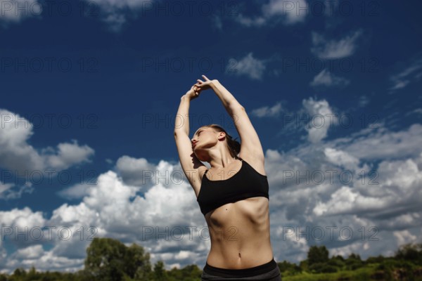 Woman stretching her arms upward with a vibrant cloudy sky