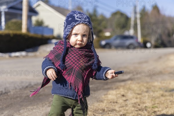 Toddler exploring his local neighborhood on a bright winter day. Portrait of 3 year old child walking alone in the street with blurry background