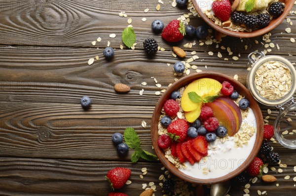 Flat lay of fruit healthy muesli with peaches strawberry almonds and blackberry in clay dish with yogurt