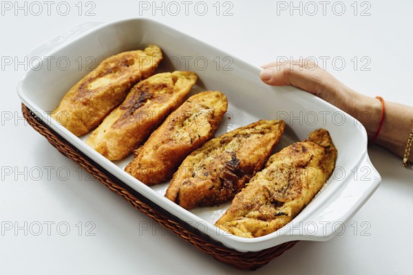Female hand holding a tray with torrijas, a typical Spanish sweet fried toasts of sliced bread soaked in eggs and milk, on white background. Traditional dessert for Lent and Easter