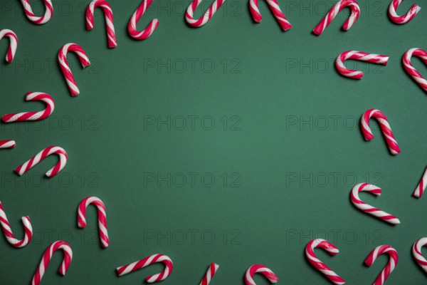 Christmas sweets frame with mini candy canes in red and white stripes, on a green paper background with empty space in the middle
