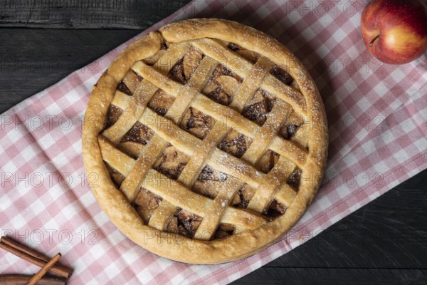 Above view of a delicious homemade apple pie with a lattice crust, on a pink towel, on a wooden table. Freshly baked desserts. National pie day