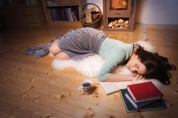 Evening image with a young beautiful woman that fell asleep while reading, on a white fur, in front of a fireplace