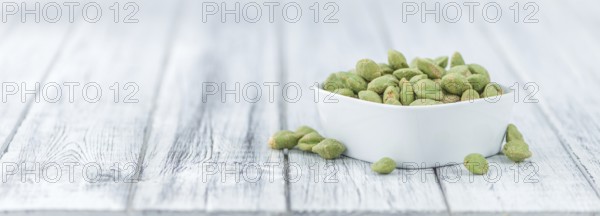 Wasabi coated Peanuts as high detailed close-up shot on a vintage wooden table (selective focus)