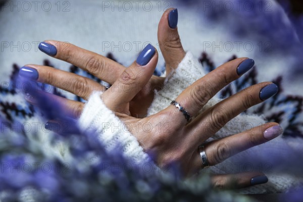 Hands showing purple manicure resting on a soft sweater, with a hint of floral elements