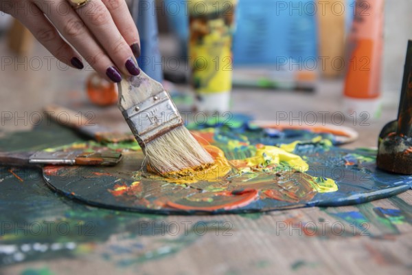 A detailed closeup of a hand skillfully mixing together vibrant and colorful paints on a palette with brushes