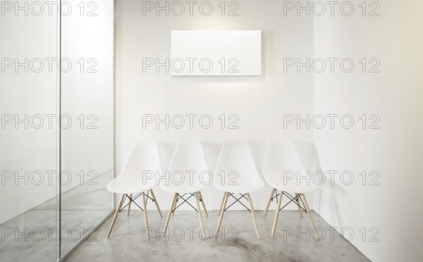 Empty office room, Glass window to the left .Loft interior style, white canvas print on the center white wall. Four white chairs at the concrete floor