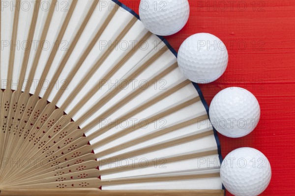 Typical Japanese hand fan made and golf balls on the wooden red table