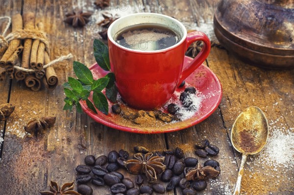 Red glass Cup with coffee on wooden background strewn with aromatic spices to drink