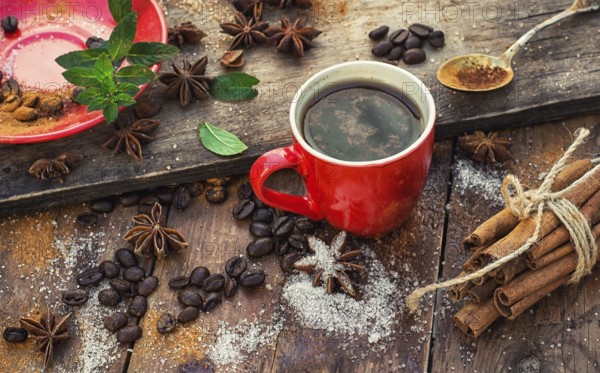 Red glass Cup with coffee on wooden background strewn with aromatic spices to drink