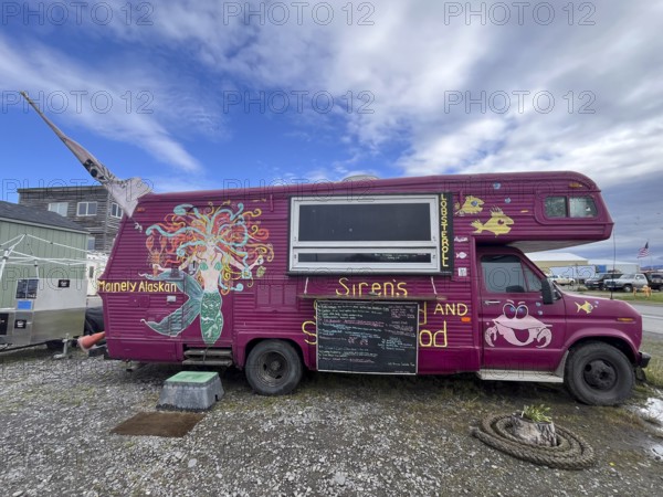 Food truck with colourful wall art and a menu in front of a cloudy street, Homer, Alaska, USA, North America
