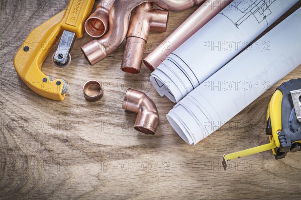 Construction drawings measuring tape copper water pipe cutter fittings on wooden board plumbing concept