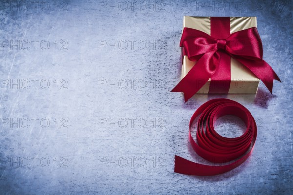 Present box with rolled red tape on metallic background copyspace