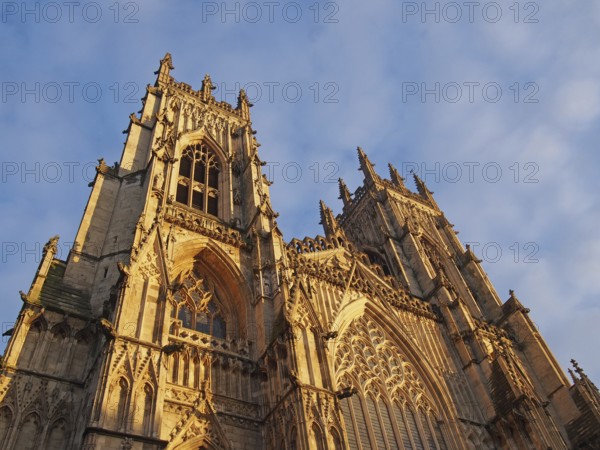 A front view of the towers at the entrance to york minster in sunlight against a blue cloudy sky