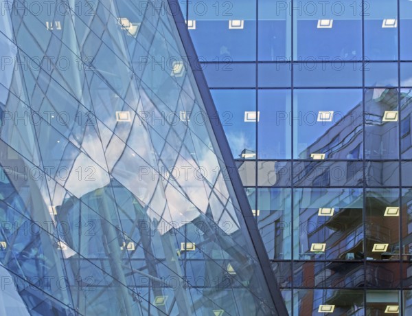 Blue sky and buildings reflected and mirrored in a large modern futuristic commercial office building