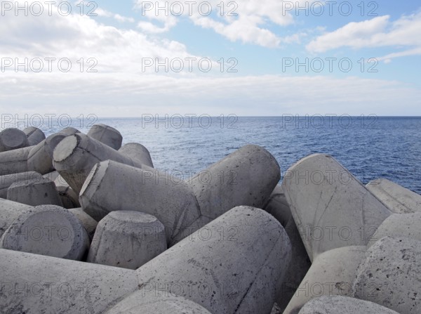 Concrete interlocking tetrapods used to prevent coastal erosion placed on a shoreline with a blue sea and sunny sky