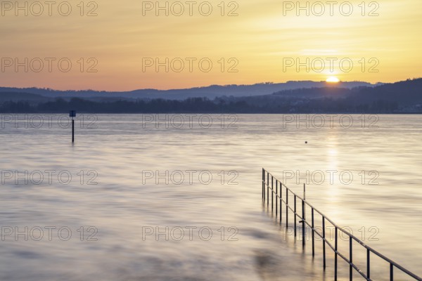 Sunrise over a calm lake with railings and distant hills, lido, Litzelstetten, Lake Constance, Baden-Württemberg, Germany, Europe