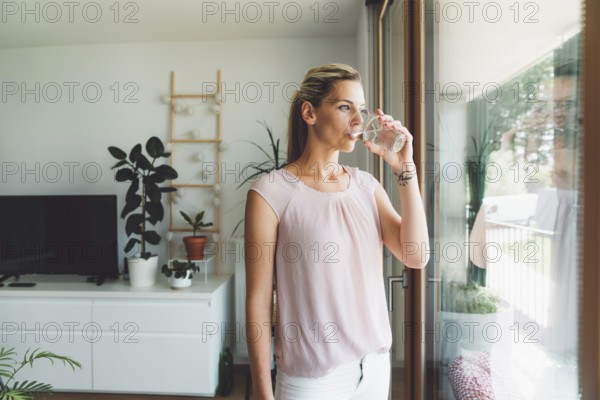 Smiling young caucasian woman taking her morning supplements, vitamin pills with a glass of water at home.