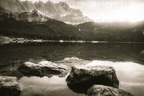 Dreamy monochrome landscape with the clear water of the Eibsee lake and the German Alps mountains reflected in it, on a sunny day of December