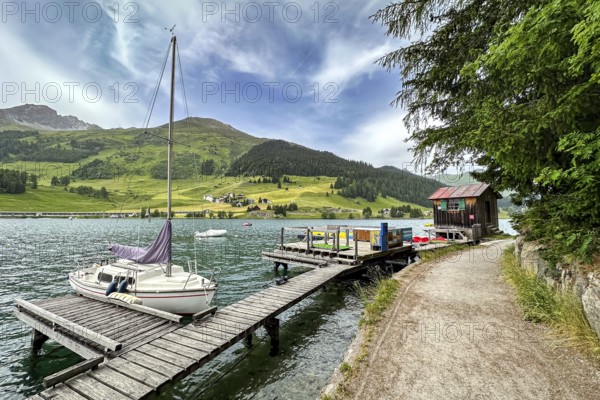 Sailing boat at a jetty on a lake, surrounded by mountains and green nature, under a cloudy sky, Davos, Switzerland, Europe