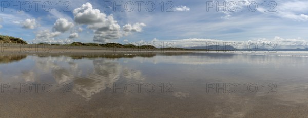 Peaceful panorama landscape of an empty golden sand beach with reflections of sky and sand dunes