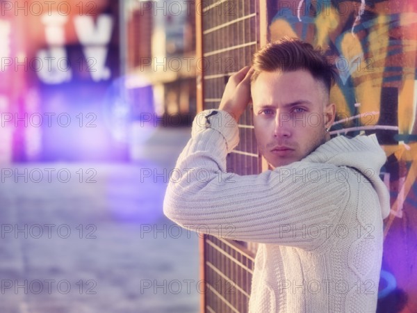 Handsome young man in city setting, with industrial site around him, looking at camera, serious expression